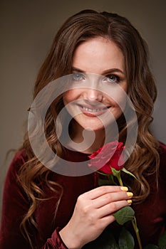 A red rose flower in the hands of a young beautiful smiling woman.