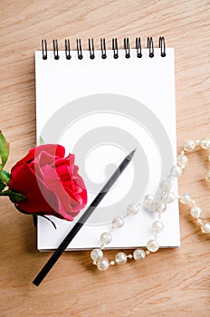 Red rose flower and pencil on blank diary.