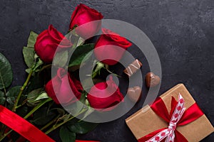 Red rose flowers bouquet, gift box, chocolate sweets on black stone background Valentine`s day greeting card