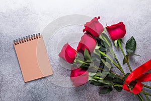 Red rose flowers bouquet, notebook on stone background Valentine`s day greeting card Copy space