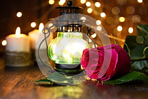 Red rose and lantern with lights on a wooden table