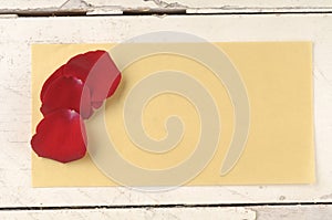 Red rose petals over paper envelope on a wooden background.