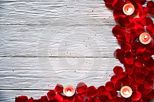 Red rose petals and red burning candles on a white wooden background.