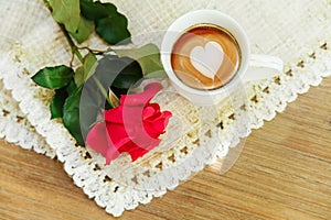 Red rose on the rough table napkin with cup of coffe.Wooden table background.Top view