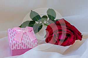 Red rose with water drops and a gift of wedding rings in a box. Linen natural color fabric background. Concept Valentine, gift,