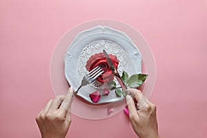 Red rose on white dish, with hand holding fork and knife, On pink background, Concept of Valentine`s Day