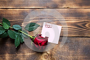 Red rose on wooden background with copyspace and sticker with a paper clip and heart, a reminder on a note sheet. Gift for woman