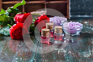 Red roses and bottles of essential oil on dark rustic background, selective focus.