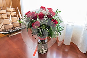 Red roses bouquet with glass vase on wooden table and curtains background