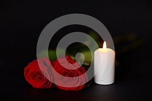 Red roses and burning candle over black background