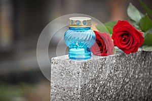 Red roses and candle on grey granite tombstone. Funeral ceremony