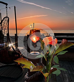 Tropical Red roses and glass of wine  with ice  on wooden table top    sunset at sea  in beach restaurant view in pink sky and se