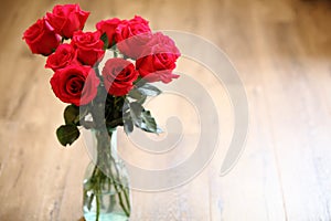 Red roses in glass vase with wooden background. Copy space