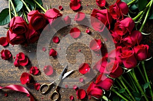 Red roses lie on the table, next to rose petals and scissors, flatleys