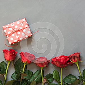 Red roses and present gift on grey background. Valentine`s card. Close up. Copy space.