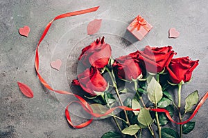 Red roses, red ribbon, red gift box on a dark grunge background. Valentine`s Day. Beautiful greeting card. Flat lay, toned