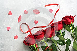 Red roses, ribbon, hearts and transparent leaves on a gray concrete background, flat lay. Valentine`s Day