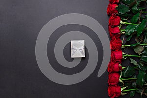 Red roses and white gift box on black colored paper background, with copy space