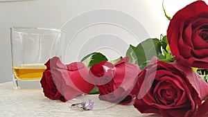 Red roses on white table near silver ring with big violet crystal