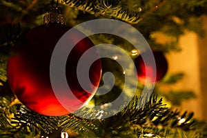 Red round Christmas ornament glistening on the tree with lights