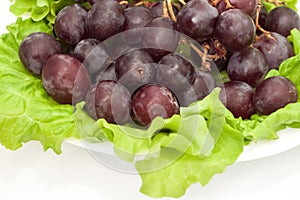 Red round grapes with salad fresh green leaves on light ceramic plate isolated white background