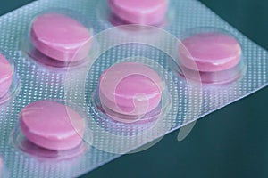 Red round pills in gray plastic packaging on a green background