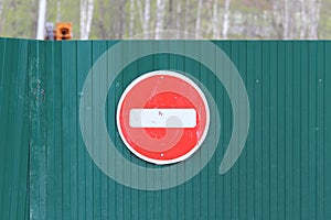 Red round road sign with white stripe prohibiting movement on the green fence of sheet iron. Do not enter. concept of