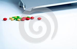 Red round sugar coated tablets and green-yellow capsules with stainless steel drug tray on white table. Pharmaceutics concept.