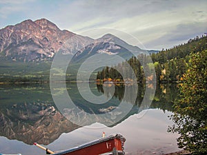 Red rowing boat in front of mirror image of Pyramid Mountain in Autumn, Rocky Mountains