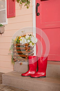 Red rubber shoes on the steps of the house.women water-proof boots.bright red gardening boots.trendy shoe for Rainy day spring,