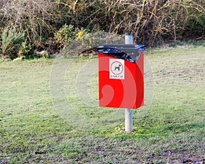 Red rubbish bin for dog`s litter with sign clean it up and picture of dog in the park