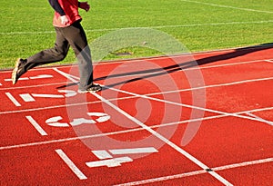 Red running racetrack on the stadium with two running legs in tracksuit trousers