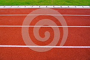 Red running track with white lines in outdoor sport stadium, side is a field and park. Backgrounds and rubber.