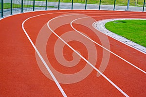 Red running track with white lines in outdoor sport stadium, side is a field and park. Backgrounds and rubber.