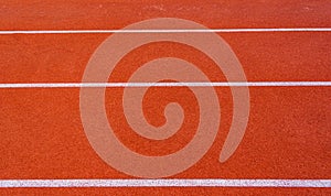 Red running track with white lines in outdoor sport stadium, side is a field and park. Backgrounds and rubber.