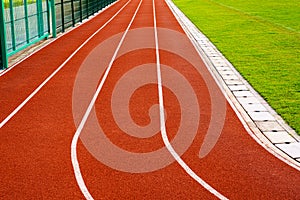 Red running track with white lines in outdoor sport stadium, side is a field and park. Backgrounds and rubber texture