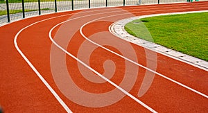 Red running track with white lines in outdoor sport stadium, side is a field and park. Backgrounds and rubber texture