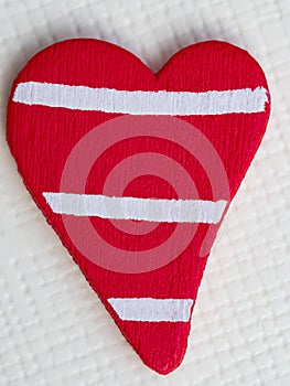 Red rustic wooden heart shape with painted white stripes, close-up