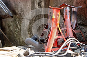 Red rusty jack stand on a table with another used engine part in a garage