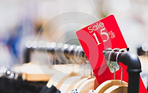 Red sale sign 15% discount on clothing rack in modern shopping mall or department store with copy space