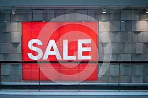 Red sale sign on clear glass store window against white wall