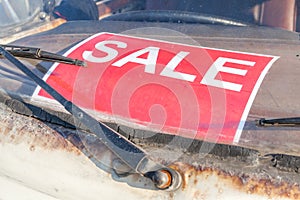 Red sale sign on grungy and old used car windshield, automobile