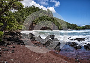 Red sand and chunks lava along the shoreline at Koki Beach on the Island of Maui in the State of Hawaii.