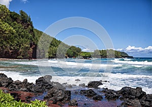 Red sand and chunks lava along the shoreline at Koki Beach on the Island of Maui in the State of Hawaii.