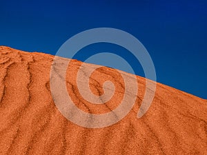 Red sand dune with ripples and blue sky.