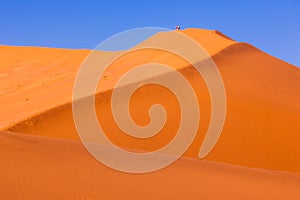 Red sand dunes with hikers in morning sunlight in Sossusvlei, Namibia