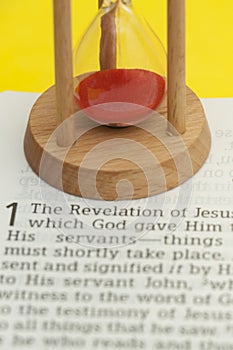Red sand hourglass on top of Holy Bible opened in Revelation of Jesus Christ Chapter 1
