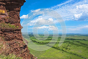 The red sandstone cliff offers a beautiful view of green meadows