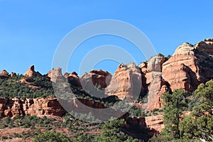 The red sandstone and white limestone mountains of Sedona with evergreen trees growing on the slopes