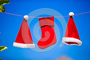 Red Santa hats and Christmas stocking hanging on tropical beach between palm trees